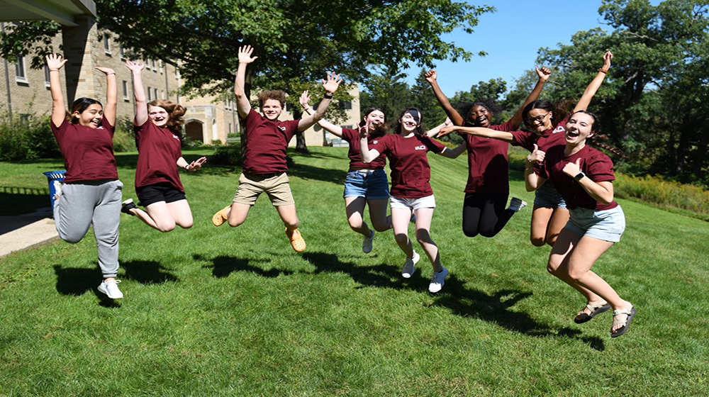 8 students outside jumping in the grass