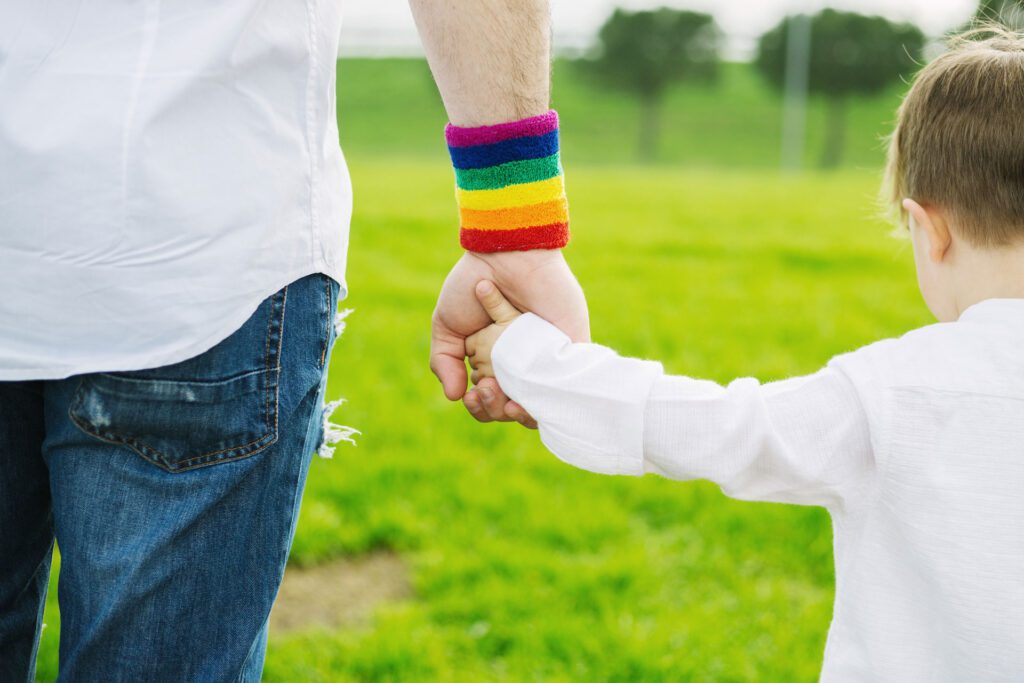 Adult with rainbow wrist band and child with white shirt walking hand in hand