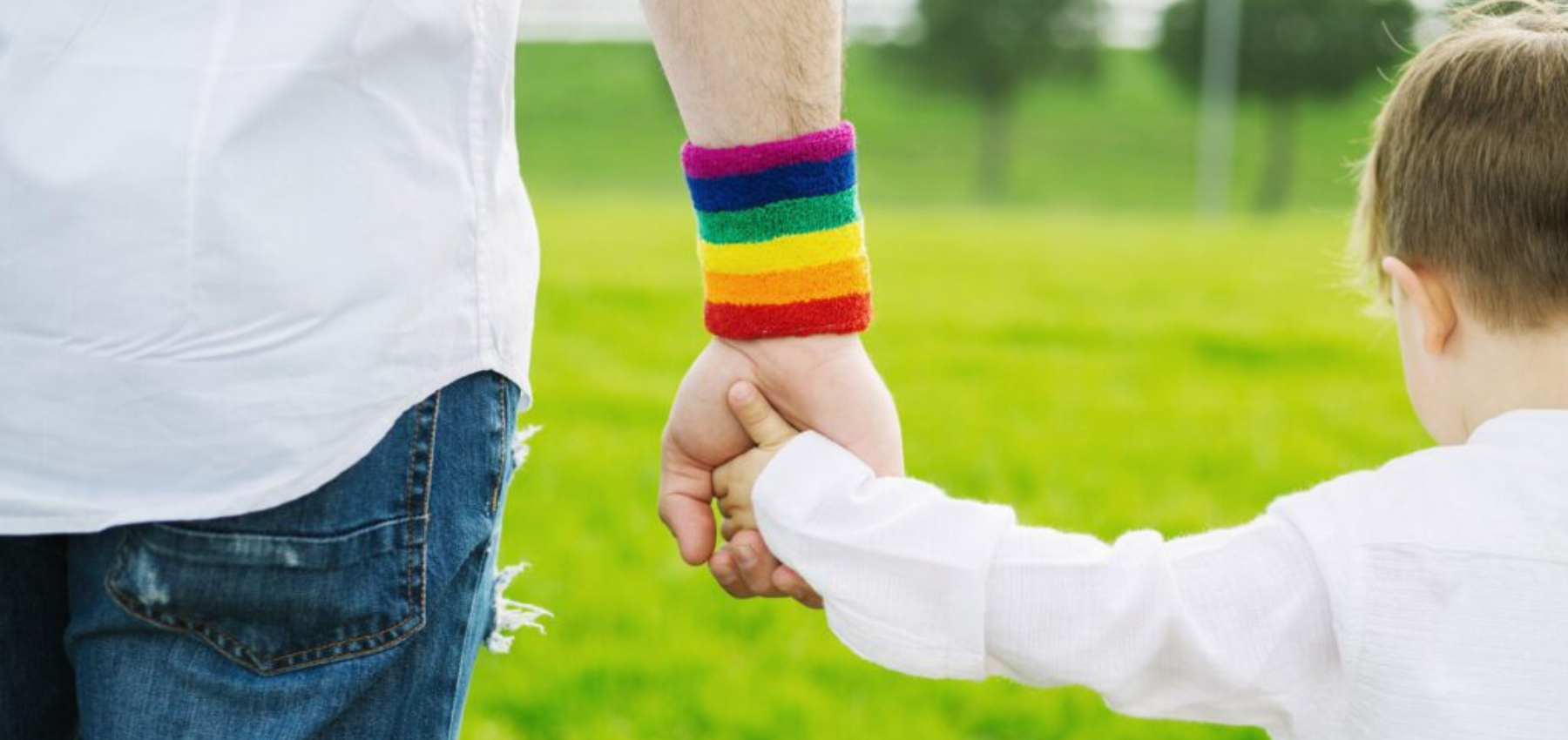 Adult with rainbow wrist band walks hand in hand with child