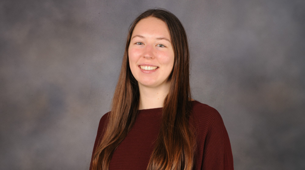 Headshot of a brunette person against a gray background