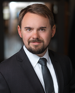 A headshot of a male with dark suitcoat and tie with white shirt