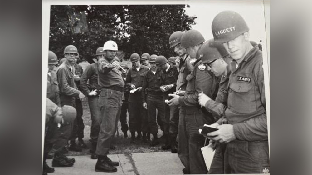 A black and white photo of Loyola University Chicago ROTC members from the 1960s. There is a large group standing in a circle around a superior