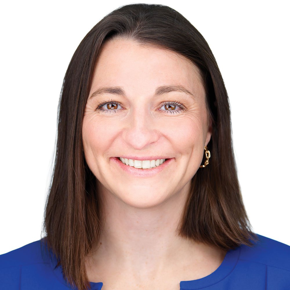 Jill McCall smiles while facing the camera wearing a blue shirt against a white background for a professional headshot.