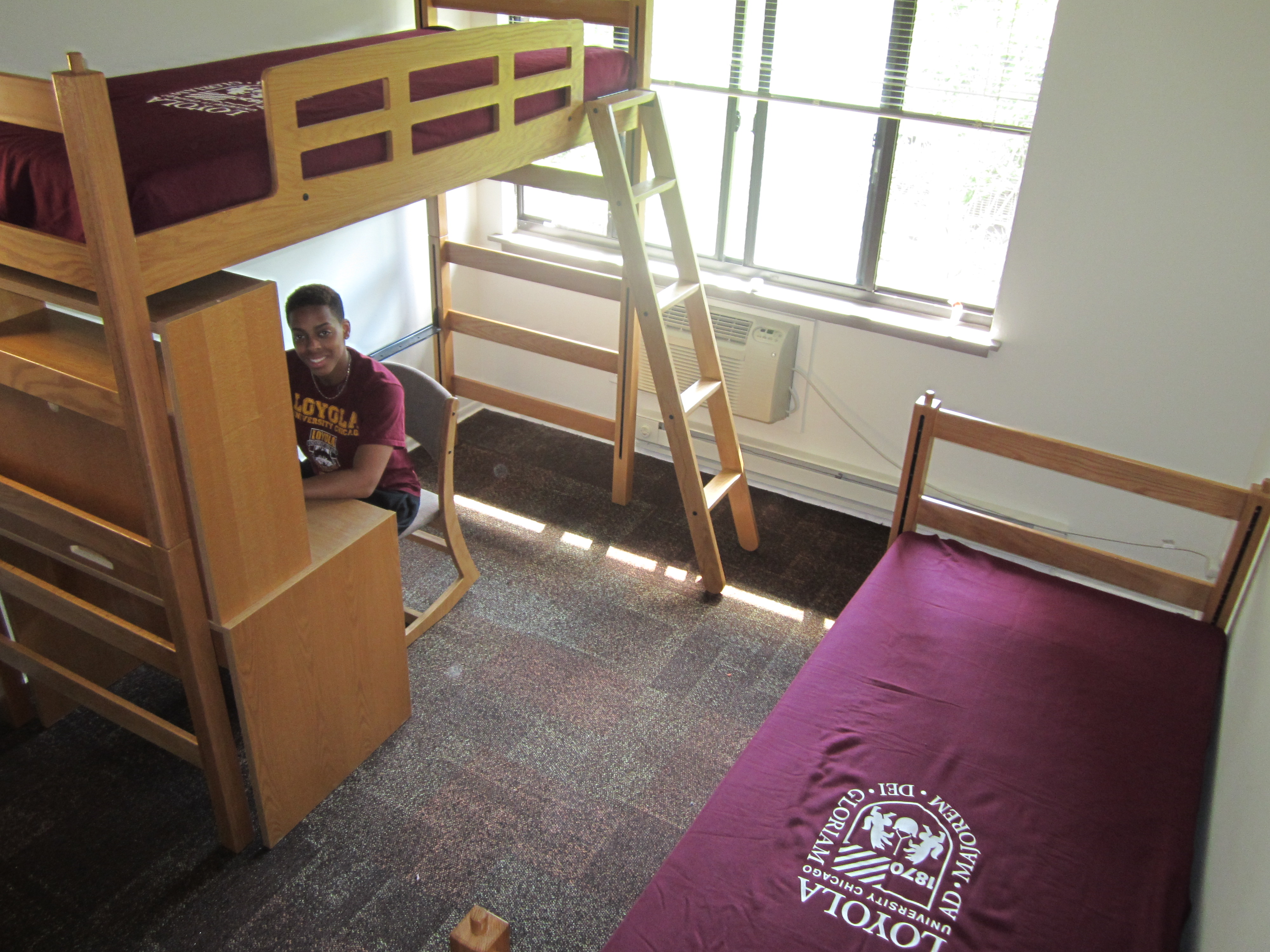 Photo of dorm room with bunk beds and a student at a desk below a bunk bed
